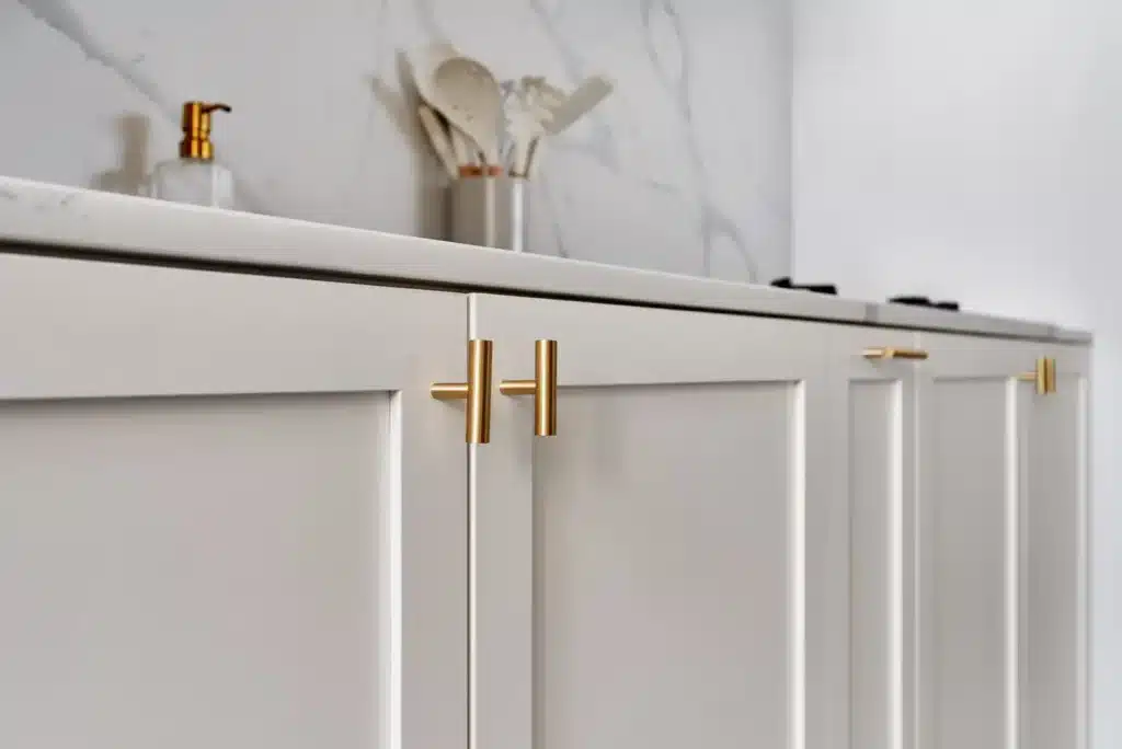 white minimalist kitchen cabinets with brass handles and marble-effect porcelain backsplash