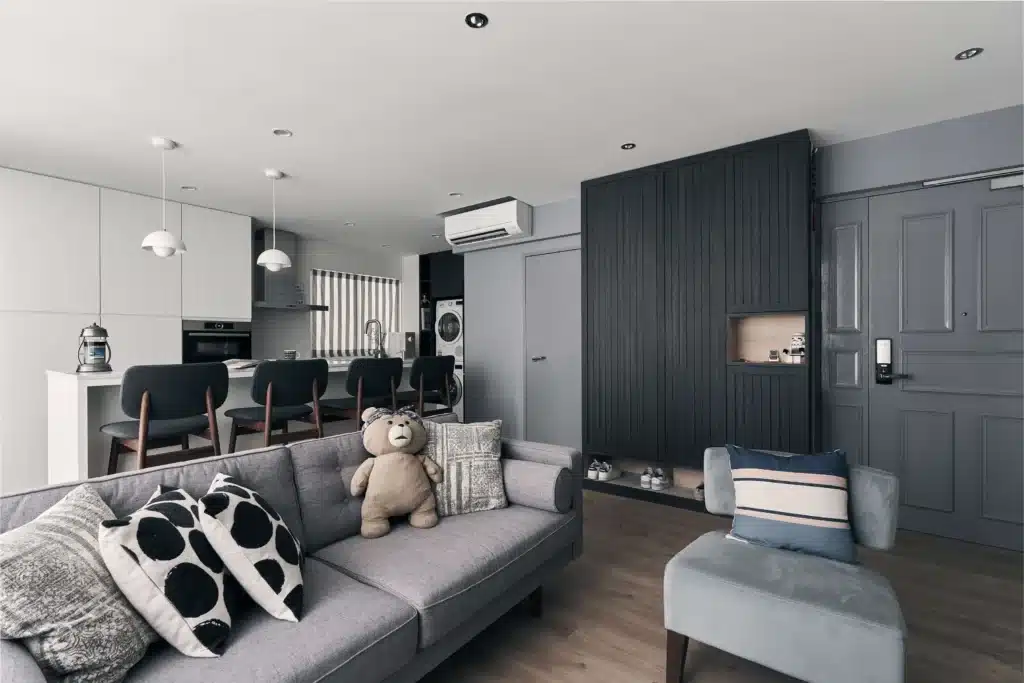 Modern open-plan living room and kitchen with grey sofa, breakfast counter and fluted storage wall by Lemonfridge Studio.