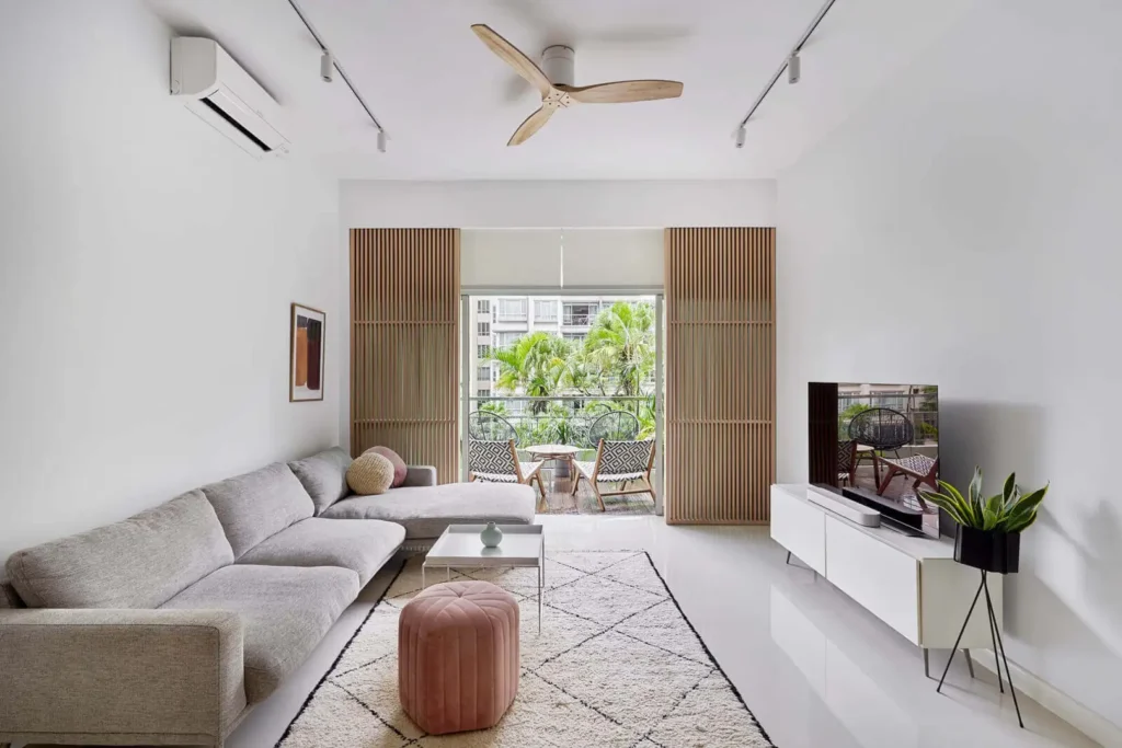 Small living room with grey sectional sofa, balcony greenery and timber screen doors in a Malaysian condo